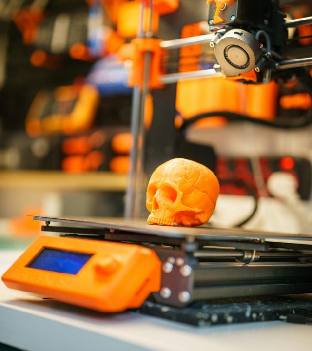 A close-up of an orange 3D printed skull on a 3D printer, showcasing modern technology in a workshop setting.
